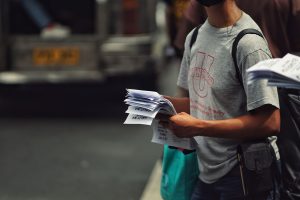 Person in casual attire distributing flyers on a busy street corner, showcasing urban life. — Coronavirus disease 2019