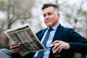 Stylish man in formal wear enjoys a drink while reading a newspaper outside. — Die besten Tischspiele im Rich Royal Casino: E