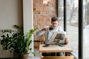 Man sitting indoors with coffee and newspaper, surrounded by plants by the window. — King Billy Casino: Mobile Wins on the Go